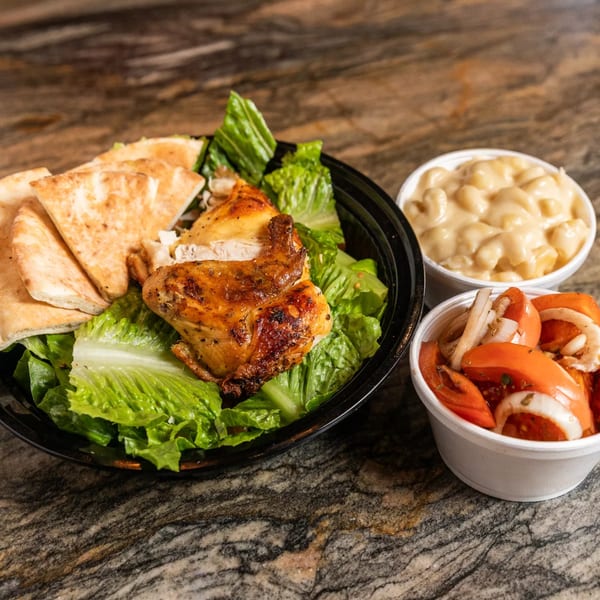 Grilled chicken leg and thigh on a bed of lettuce with pita bread, mac and cheese, and tomato salad.