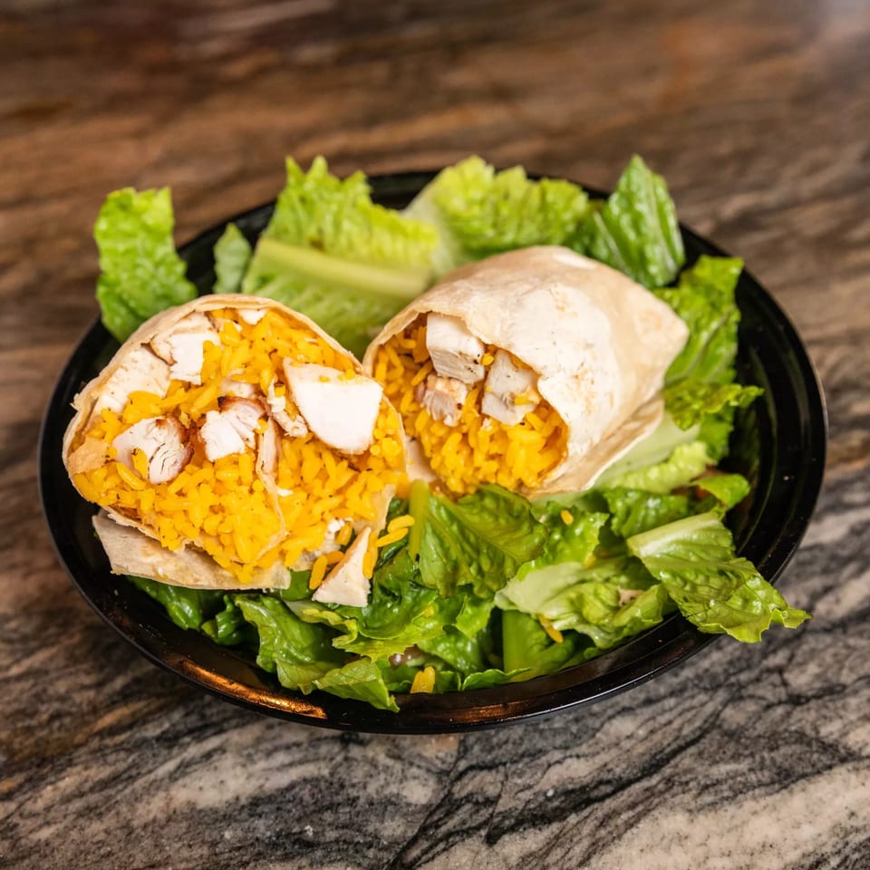 Two grilled chicken and yellow rice burritos, cut in half, served on a bed of fresh lettuce.