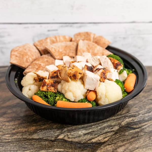 Grilled chicken pieces, broccoli, cauliflower, and carrots in a black bowl with pita bread.