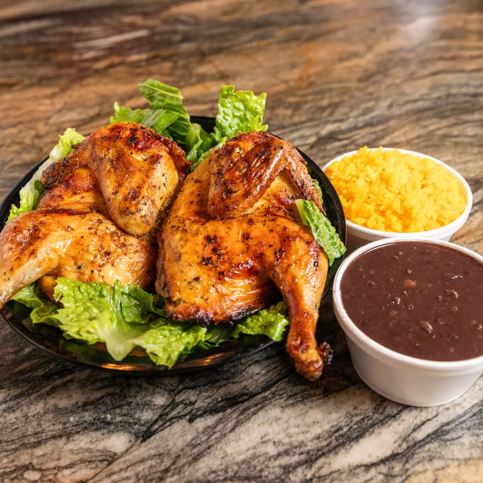 Two halves of grilled chicken on lettuce, with yellow rice and black beans on a marble surface.