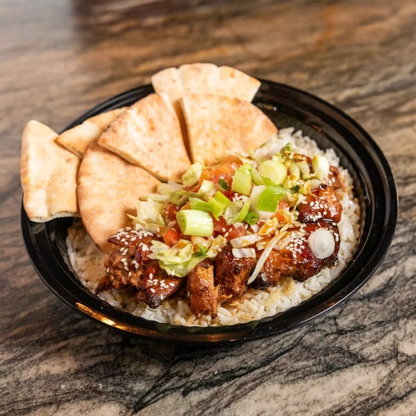 Grilled chicken and rice bowl with pita bread, topped with green onions, tomatoes, and sesame seeds.