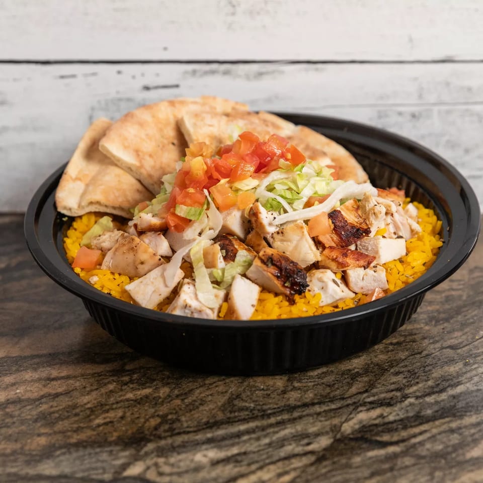 Grilled chicken and yellow rice bowl topped with diced tomatoes, lettuce, and pita bread.