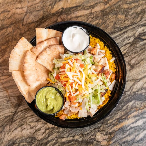 Grilled chicken bowl with yellow rice, shredded lettuce, cheese, tomatoes, pita bread, guacamole, and sour cream.