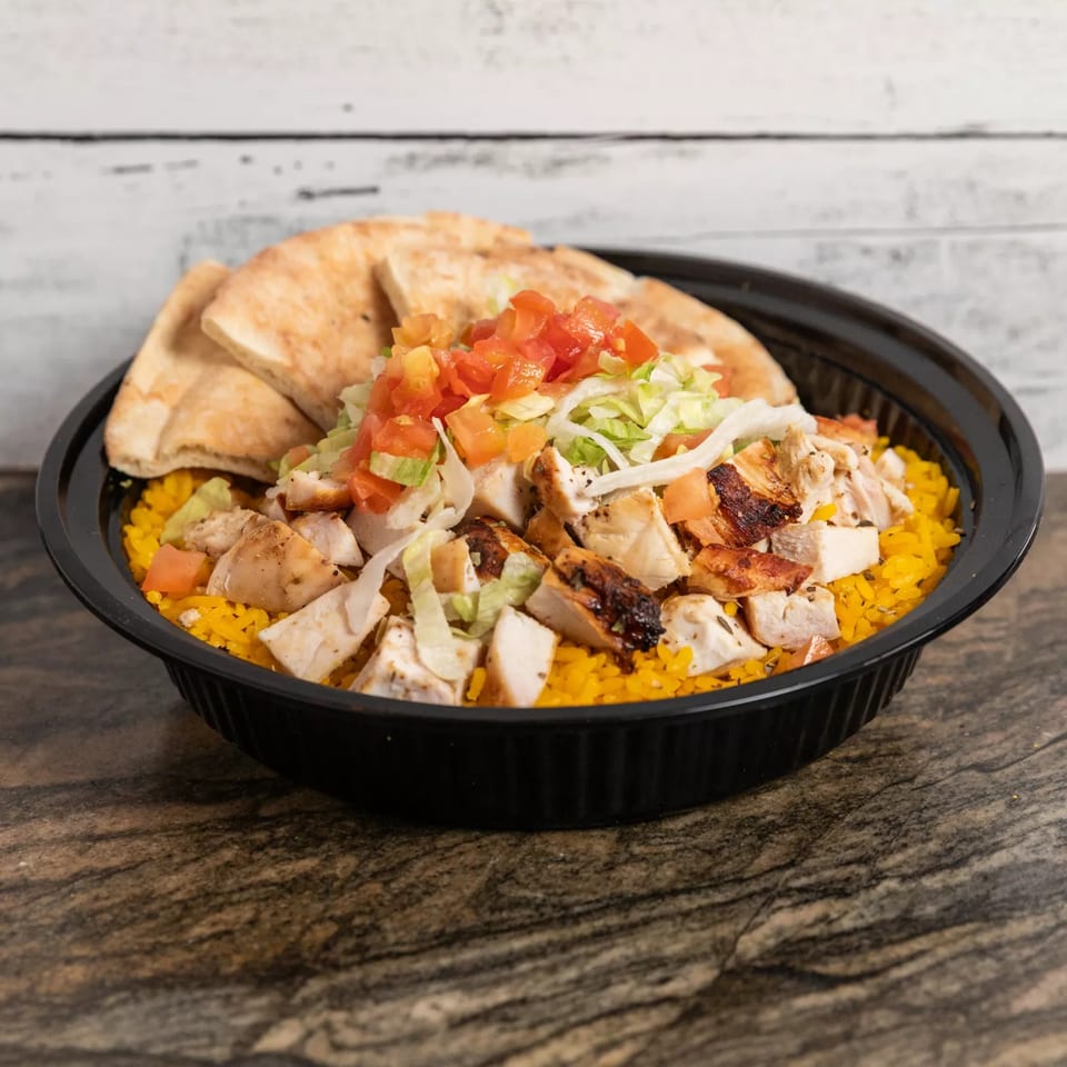 Grilled chicken and yellow rice bowl with pita bread, diced tomatoes, and shredded lettuce.